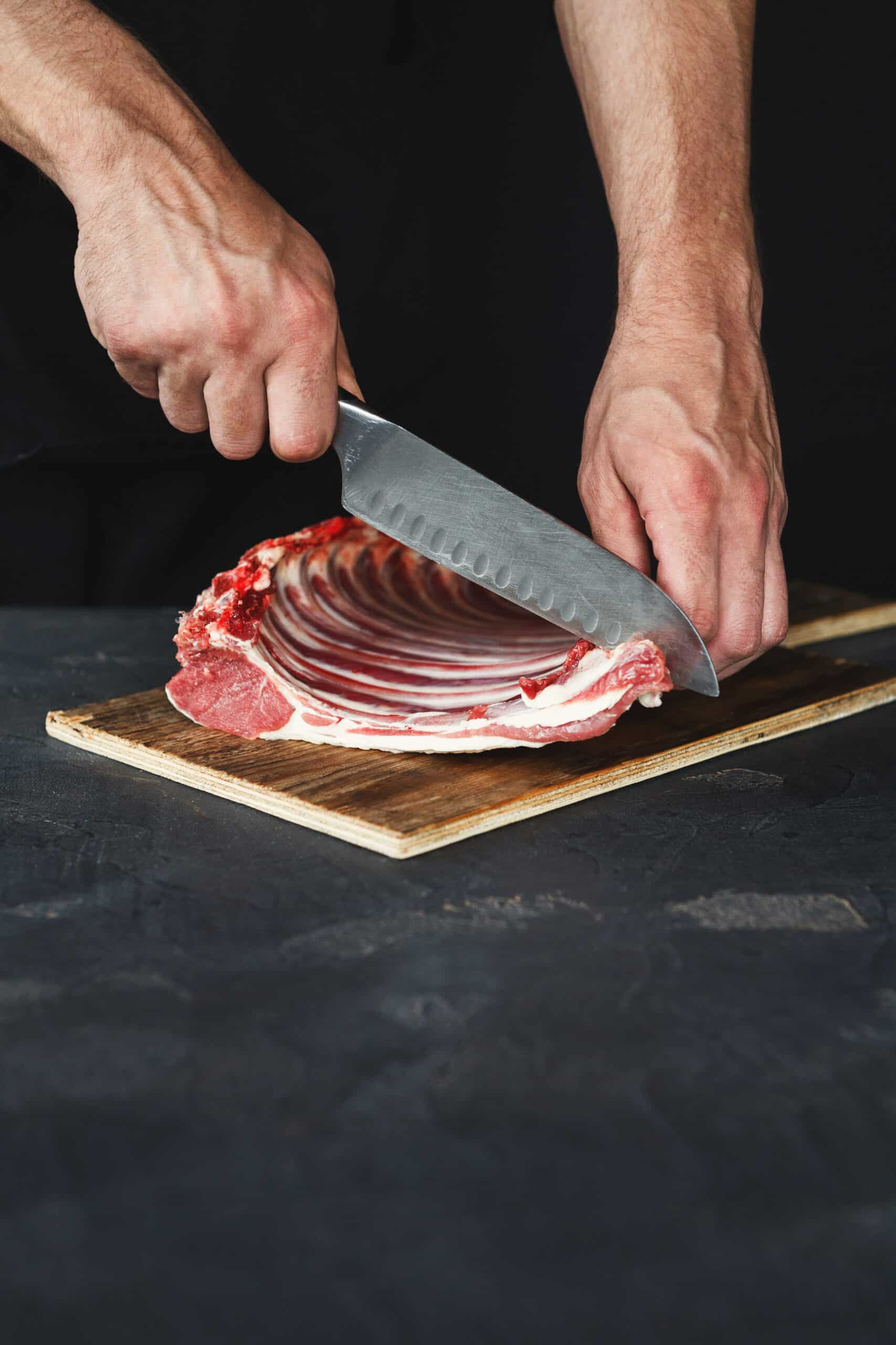 Chef cutting rack of lamb on wooden board in kitchen
