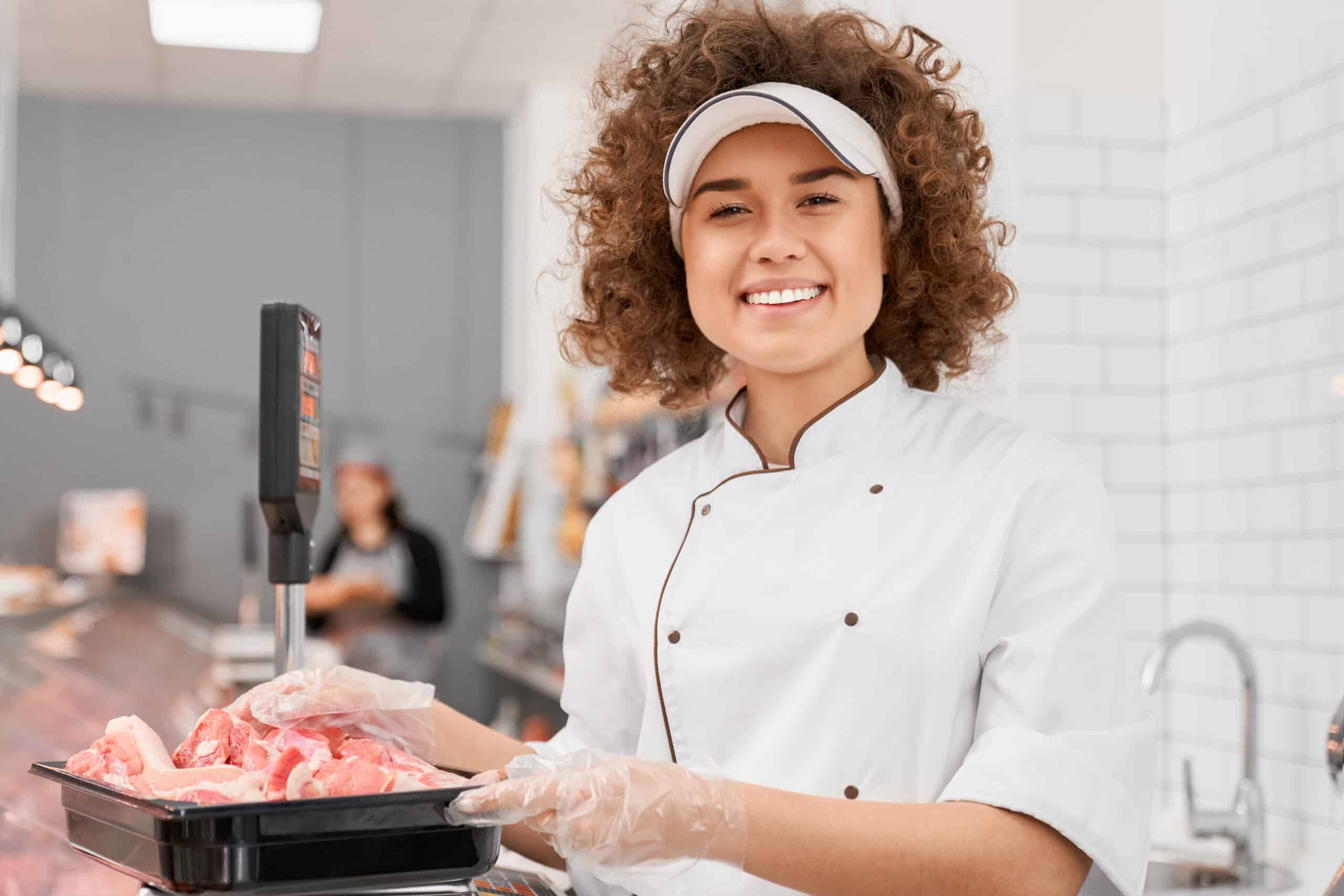 Shop worker weighing meat on scales.